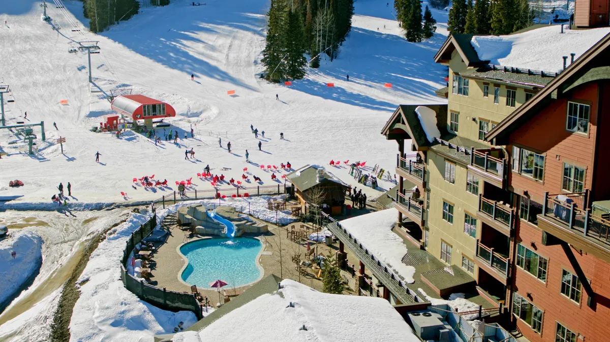 A vibrant exterior shot capturing the lodge’s swimming pool, nearby ski slopes, a ski lift, and the lodge architecture. The energy of guests swimming and the festive atmosphere provide a sense of fun and activity right at your doorstep.