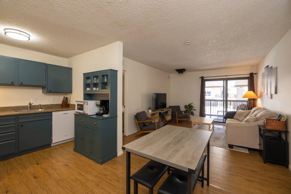 A view of the open-concept kitchen, dining area, and adjacent seating area with a balcony door. The layout is spacious, allowing easy flow between the living, dining, and kitchen spaces.